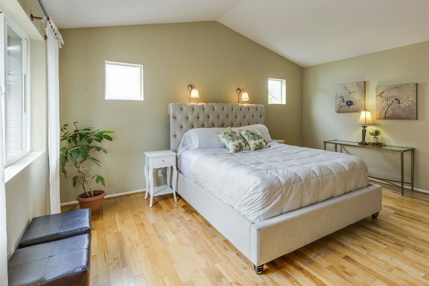 A white upholstered bed, bedside lamps and green accents in a bedroom with wood flooring.