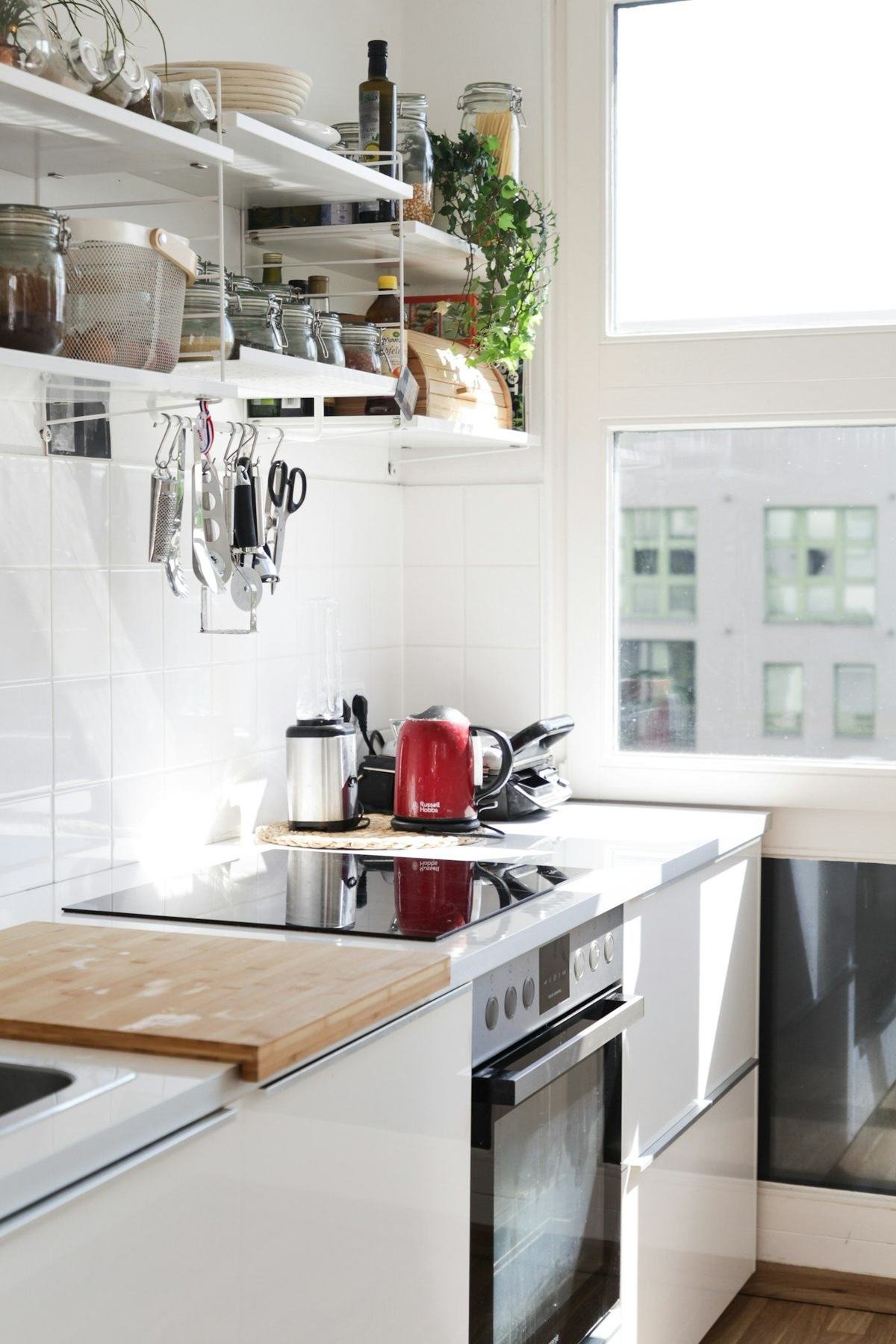 A bright white kitchen with a wooden worktop, open shelving and plants beside a window.