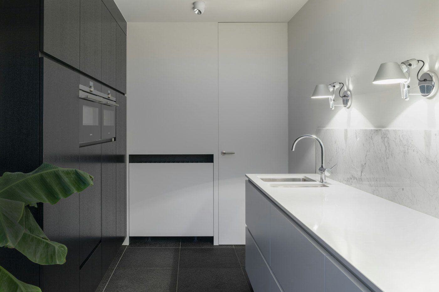 A white kitchen counter and sink with wall-mounted lamps and a marble backsplash.
